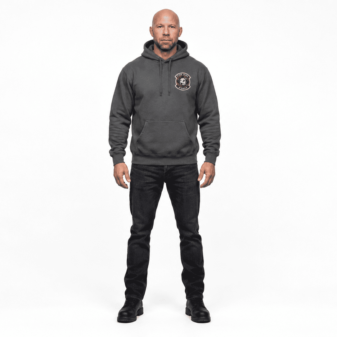 A bald man wearing a dark gray pullover hoodie with a circular black and white graphic on the left chest, paired with black jeans and black boots, standing against a solid white background.